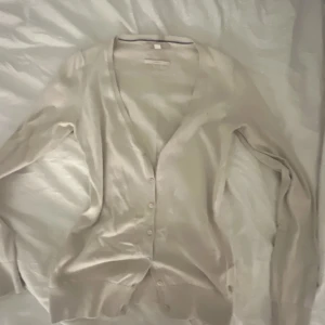 Beige kofta med knappar - Säljer en stilren beige kofta i mycket bra skick. Den har en v-ringad design och knappar framtill. Perfekt för både vår och höst, och passar till många olika outfits. Supermjuk och bekväm att ha på sig!