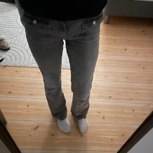 Gråa bootcut jeans - Säljer ett par grå jeansbyxor i bra skick. De har en klassisk femficksdesign med knappar och dragkedja framtill. Perfekta för vardagsbruk och kan matchas med det mesta i garderoben. Passformen är normal och de är bekväma att ha på sig hela dagen.💘
