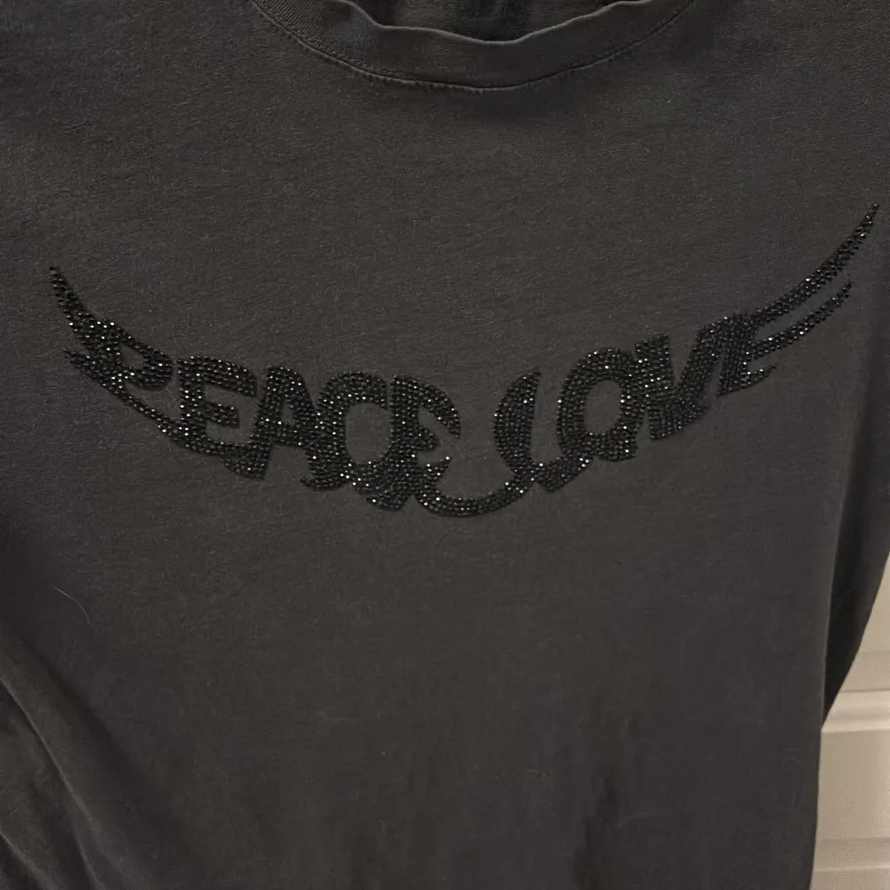 Säljer en svart/grå t-shirt från Zadig & Voltaire med texten 'Peace Love' i glittriga bokstäver på framsidan. T-shirten har en klassisk rund hals och korta ärmar🖤 köparen betalar frakten!. T-shirts.