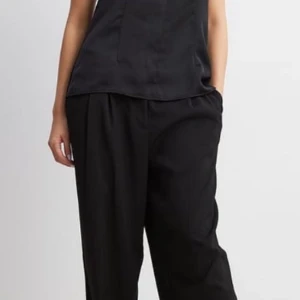 Svart halterneck linne - Snyggt svart halterneck linne med öppen rygg och knytband i nacken. Perfekt för en utekväll eller fest. Materialet ser ut att vara mjukt och glansigt, vilket ger en elegant touch.