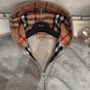 Burberry hoodie - Säljer en snygg grå hoodie från Burberry i Stl XL men passar L skulle jag säga. Den är i bra skick förutom ett litet stygn som gått upp men som går att sy igen lätt och smidigt. Perfekt för höst och vår, och passar både till vardags och lite finare tillfällen. Obs:skriv innan köp. Priset ej hugget i sten