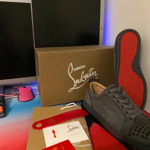 Grå mockasneakers från Christian Louboutin - Hej jag säljer nu ett par grå sneakers i mocka från Christian Louboutin. Skorna har en cool design med svarta nitar på tån och klassisk röd sula. De är i nytt skick och kommer med originalförpackning och tillbehör. Nypris ca 9000kr. Bara höra av dig om du har några frågor!