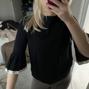 Svart topp med volangärmar - Snygg svart topp med trekvartsärm och volangdetaljer i vitt vid ärmsluten. 