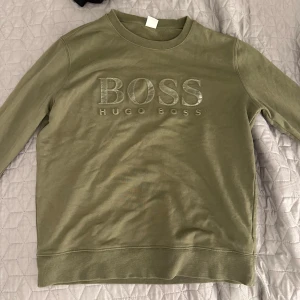 Olivgrön tröja från Hugo Boss - Säljer en snygg olivgrön tröja från Hugo Boss med deras ikoniska logga broderad på framsidan. Tröjan har en normal passform och är perfekt för både vardag och avslappnade tillfällen. Den är i mycket bra skick och redo för en ny ägare!