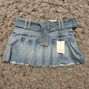 Jeanskjol från Zara - Superfin jeanskjol från Zara i ljusblå denim. Kjolen har fina volanger som är supersnyggt . Den har en låg midja och kommer med ett matchande bälte. Perfekt för sommardagar eller en avslappnad utekväll. Helt ny med tag kvar!