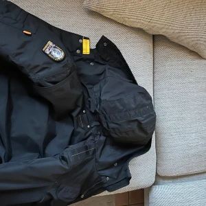 Svart jacka från Parajumpers nypris 10000 slusåld nästan överallt masterpiece series äkta - Säljer en svart Parajumpers jacka i mycket bra skick. Den har en quiltad insida och en snygg patch på ärmen. Jackan är perfekt för höst och vinter med sin varma och skyddande design. Den har en dragkedja och flera praktiska fickor. Perfekt för dig som vill ha både stil och funktion! Äkta
