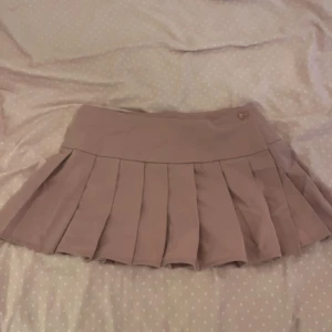 rosa plisserad kortkjol - Säljer en superfin rosa plisserad kortkjol. Den har en knappdetalj i midjan. 