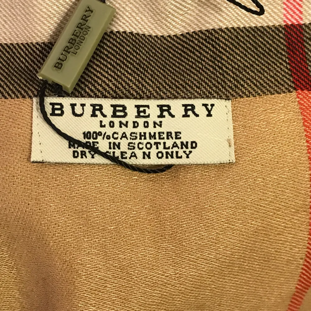 Säljer en klassisk beige rutig halsduk från Burberry i 100% kashmir. Den är supermjuk och perfekt för att hålla dig varm under höst och vinter. Den har det ikoniska rutmönstret i svart, vitt och rött. Tillverkad i Skottland och i mycket bra skick. Perfekt accessoar för en stilren look!. Accessoarer.