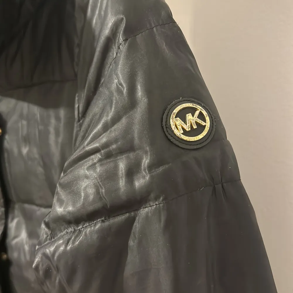 Säljer en snygg svart pufferjacka från Michael Kors. Jackan har en stilren design med guldiga dragkedjor och knappar. Perfekt för kyliga dagar med sin varma vaddering. Den har långa ärmar och en hög krage för extra skydd mot kylan. Passar både till vardags och lite finare tillfällen.. Jackor.