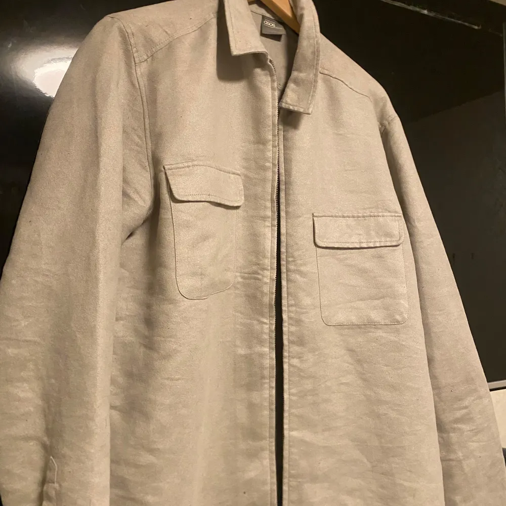 Säljer en snygg beige overshirt från asos. Den har en dragkedja framtill och två praktiska bröstfickor med lock. Perfekt för lager-på-lager-stil under hösten eller våren. Materialet känns slitstarkt och bekvämt. Passar både till vardags och lite mer uppklädda tillfällen. 🧥✨. Jackor.