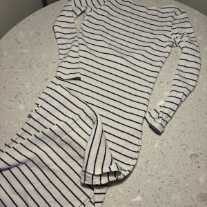 Randig klänning från NA-KD - Säljer en superfin randig klänning från NA-KD i storlek M. Den är vit med mörkblå ränder och har en öppen rygg som ger en snygg detalj. Klänningen är ribbad och långärmad, och har en slits. perfekt för både vår och sommar. Passar till både vardag och fest!