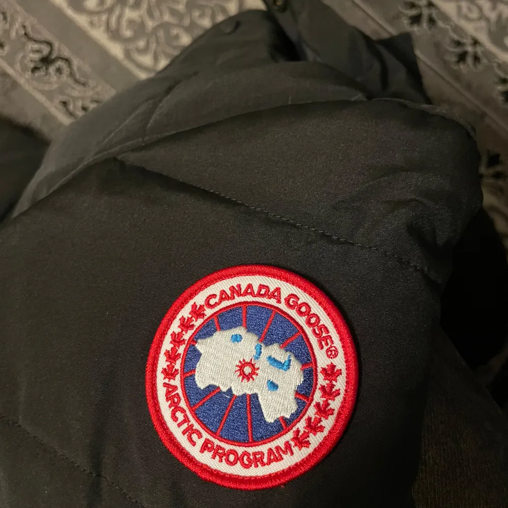 Säljer en svart dunjacka från Canada Goose i mycket bra skick. Jackan har en pälskantad huva och är perfekt för kalla vinterdagar. Den har långa ärmar och en snygg logga på ärmen. Passar både till vardags och mer äventyrliga aktiviteter. Håll dig varm och stilren i vinter! ❄️. Jackor.