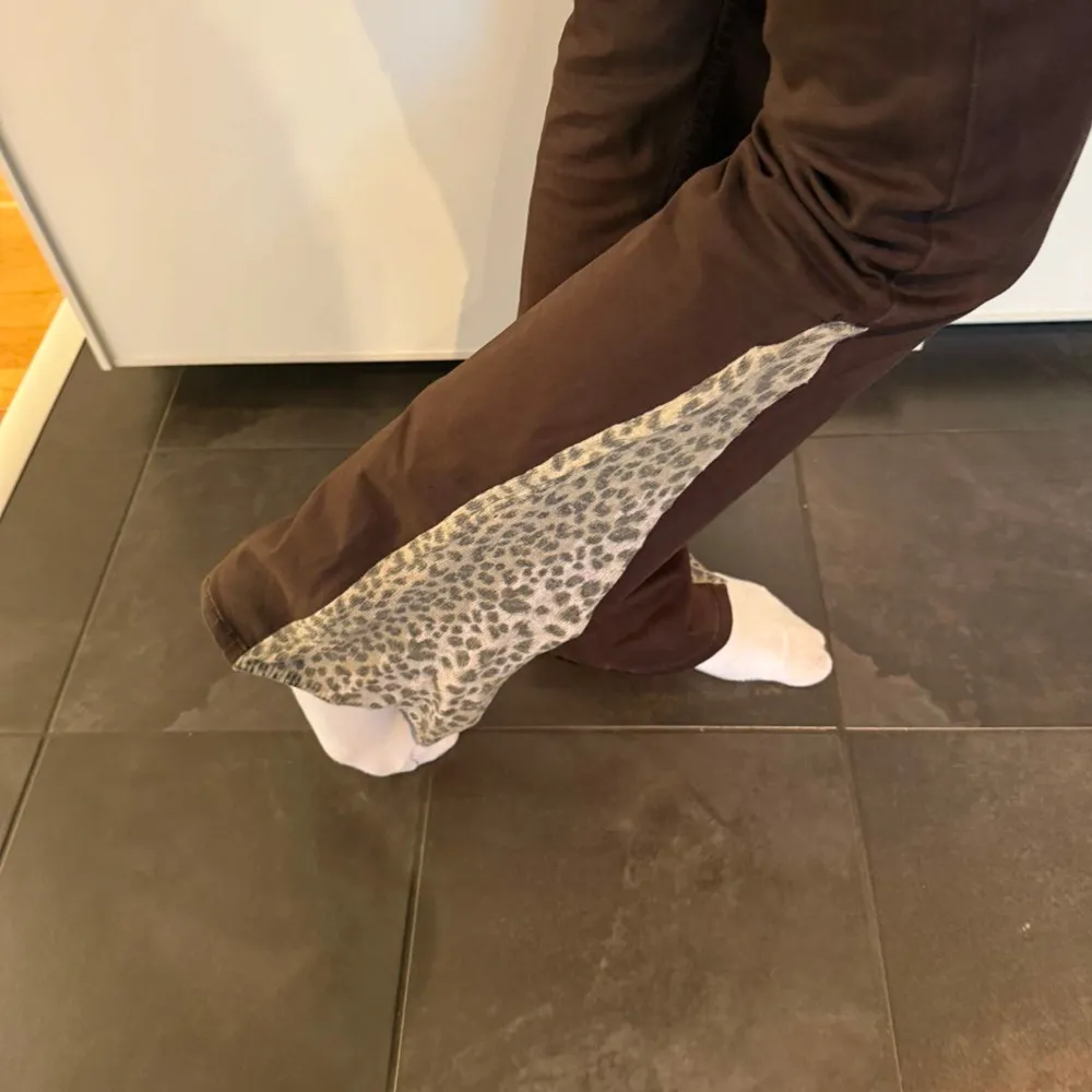 Säljer ett par snygga bruna bootcut byxor med leopardmönstrade detaljer längs sidorna. Byxorna har låg midja och är dekorerade med pärlor på bakfickorna. Perfekta för en unik och trendig look! Midja: 34,5 cm Innerbenslängd: 82 cm Ytterbenslängd: 105 cm. Farkut & Housut.