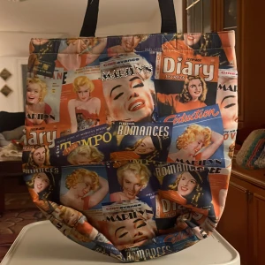 Färgglad shoppingväska med retrotryck - Säljer en supercool shoppingväska med retrotryck av tidningsomslag i olika färger. Väskan har svarta handtag och är perfekt för en dag på stan eller som en unik accessoar. Den är rymlig och har en öppen design utan dragkedja. Perfekt för dig som älskar vintage och vill sticka ut!