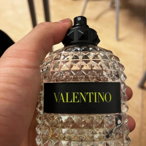 Valentino yellow dream - Säljer en snygg parfymflaska från Valentino. Flaskan är genomskinlig med ett coolt mönster av små pyramider och har en svart etikett med gult tryck. Korken är svart och stilren. Perfekt för den som vill ha en lyxig touch på sin parfymhylla!
