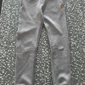 Grå mjukisbyxor från Lyle & Scott - Säljer ett par oanvända endast prövade grå mjukisbyxor från Lyle & Scott i storlek 10-11 år. Byxorna är i mjukt material och har en liten logga på sidan. Perfekta för en avslappnad dag hemma eller för sportaktiviteter. De är i nyskick och redo för en ny ägare!