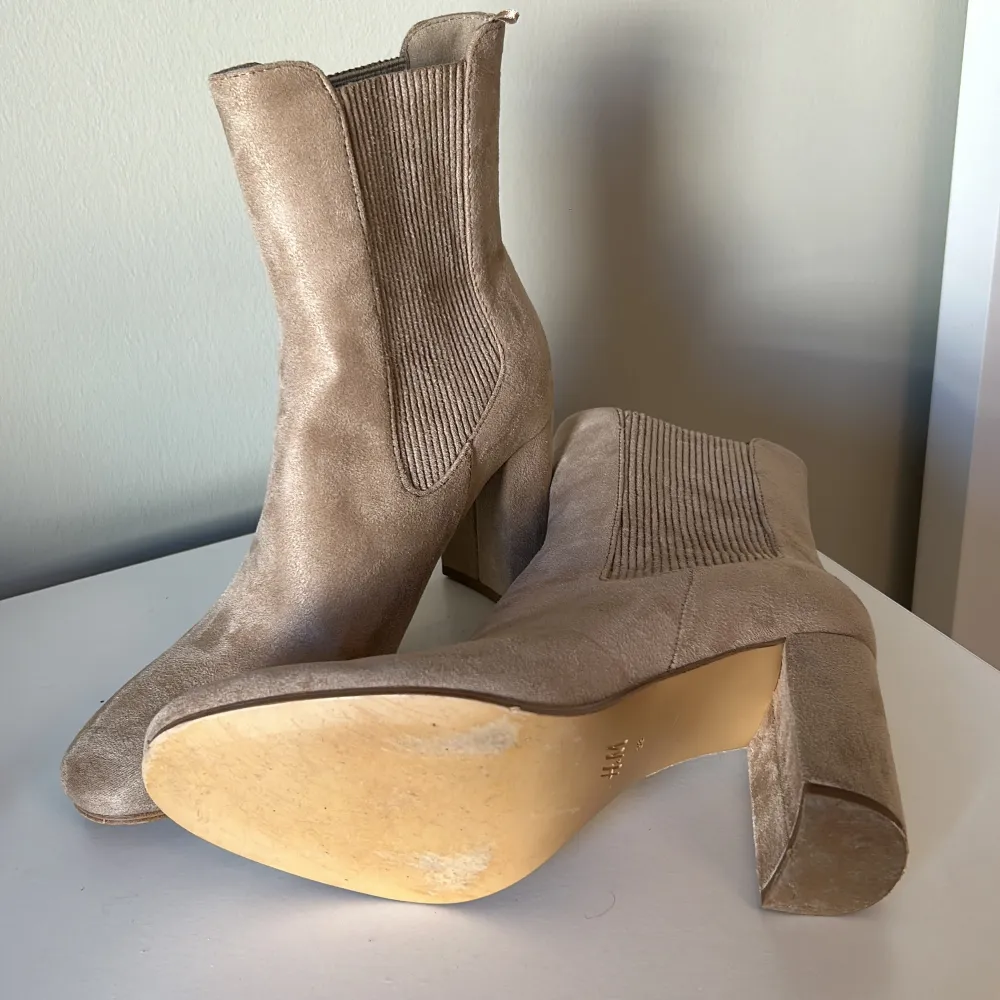 Säljer ett par snygga beige stövletter i mocka. De har en stilren design med en bekväm klack och elastiska paneler på sidorna för enkel på- och avtagning. Perfekta för både vardag och fest!. Kengät.