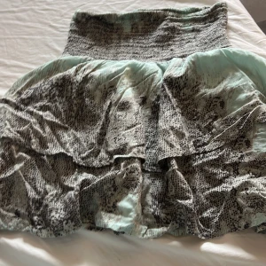 Mönstrad kjol från Vila - Säljer en superfin kjol från Vila i storlek M. Kjolen har ett coolt mönster i grått och ljusblått med volanger som ger en härlig volym. Perfekt för både vardag och fest! 🖤