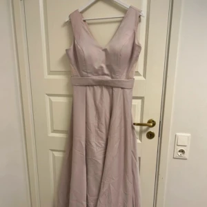 Ljuslila långklänning  - Ljuslila långklänning med v-ringning och genomskinliga öppningar vid sidan. Liten i storleken, passar 38.