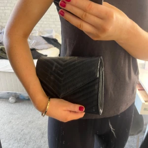 Svart quiltad kuvertväska - Säljer en stilren svart kuvertväska/clutch med quiltat mönster. Perfekt för en utekväll eller fest! Väskan är i syntetmaterial och har en elegant design som passar till alla outfits.