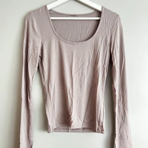Beige långärmad topp - Säljer en stilren beige långärmad topp i mjukt material. Toppen har en rundad hals och en liten slitsdetalj vid ärmsluten. Perfekt för både vardag och fest!