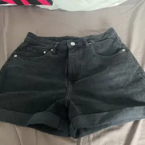 Säljer ett par svarta mom shorts från H&M i storlek 36. De är i denim och har en ultra hög midja, perfekt för en avslappnad och trendig look. Shortsen har klassiska fem fickor och en knappgylf. Perfekta för sommardagar eller en casual utekväll!