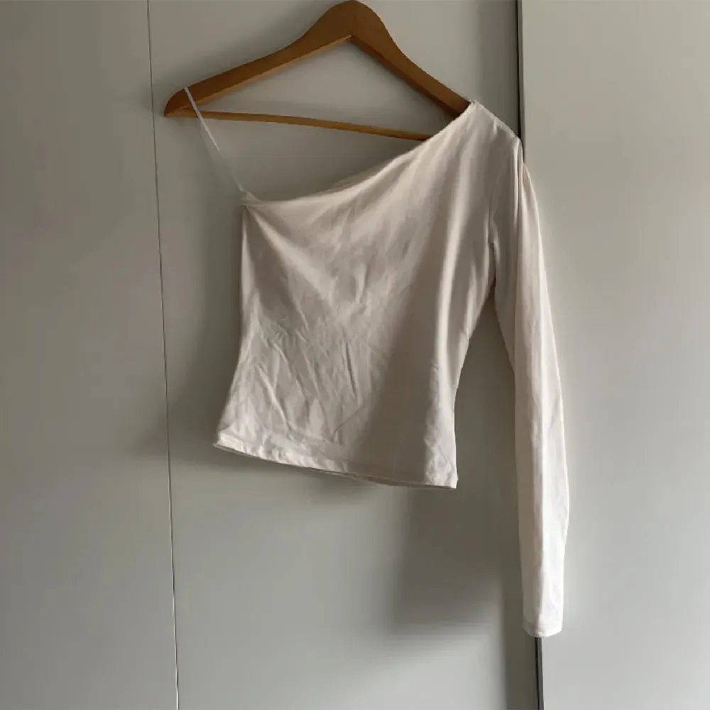 Säljer en stilren créme vit oneshoulder topp från H&M. Drömlikt material❤️. Toppar.