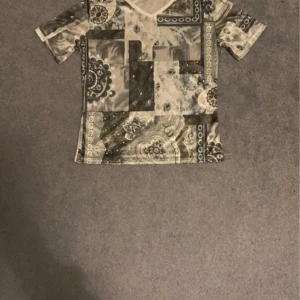 Blågrå T-shirt Indiskt Mönster  - Fin och unik ”t-shirt”i silke material. Mönstret är patchwork med indisk inspiration. Sitter bra och är väldigt skön och mysig. Knappt använd, inga synliga tecken på slitage.  Köp direkt eller lägg prisförslag.  Skickar vanligtvis inom 1-2 dagar. 