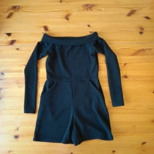 Svart offshoulder jumpsuit - Säljer en stilren svart jumpsuit med offshoulder-design och långa ärmar. Perfekt för en festlig kväll eller en utekväll med vänner. Den har en tight passform som framhäver figuren.