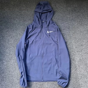 Blå vindjacka från Nike - Säljer en blå vindjacka från Nike med huva och dragkedja. Perfekt för blåsiga dagar och har en stilren design med Nike-loggan på bröstet. Jackan är långärmad och har en normal passform.