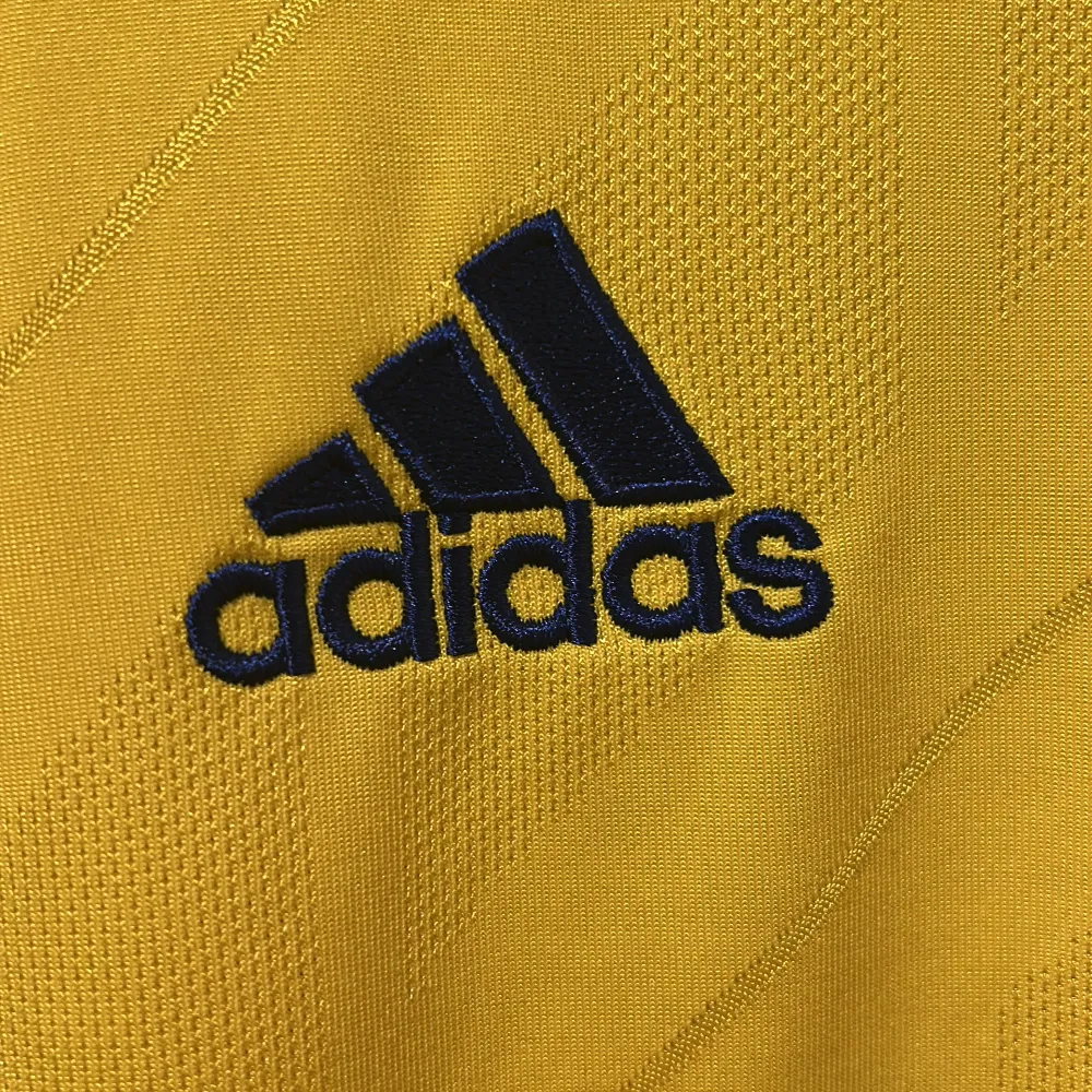 Säljer en svensk landslags fotbollströja från Adidas med Sveriges landslagsemblem på bröstet. Tröjan har korta ärmar och en blå randig detalj på sidorna. Perfekt för fotbollsfans som vill visa sitt stöd för Sverige! 🟡🔵. T-shirts.