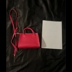 Rosa väska  - En fyrkantig mindre handväska som aldrig använts! (Mäter den genom ett A4 papper på bild så man ser ungefär hur stor den är😊) axelband medföljer!❤️