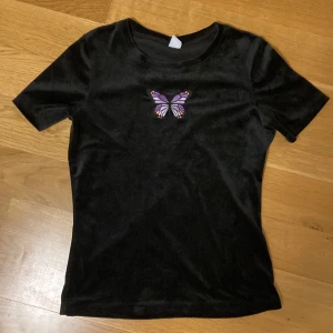 T-Shirt med fjäril - Svart lite fluffig T-shirt med en lila fjäril på