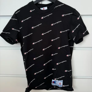 Svart t-shirt från Champion - Snygg svart t-shirt från Champion med ett all-over tryck av deras logga. Använd ett fåtal gånger 🌸