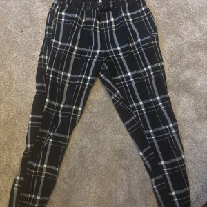Svarta rutiga byxor från Björn Borg - Snygga svarta byxor med vitt rutmönster från Björn Borg. Perfekta för en avslappnad stil med elastisk midja för extra komfort. Tillverkade i ett mjukt material som känns skönt mot huden.