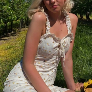 Vit blommig klänning med volangdetaljer - Vit klänning med små gula/rosa blommor och volangdetaljer. Den har en knytning framtill och axelband med volanger. Såå fin men tyvärr har jag växt ur den 💛