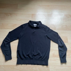 Svart pikétröja från These Glory Days - Snygg svart pikétröja från These Glory Days i superior bomull. Tröjan har en klassisk krage med knappar och långa ärmar. Perfekt för en stilren look.