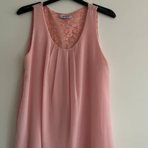 Rosa ärmlös topp från MyHailys - Säljer en söt rosa ärmlös topp från MyHailys med spetsdetaljer vid halsen och en öppen rygg. Perfekt för varma dagar eller som ett lager under en kavaj. Toppen har en luftig passform och är gjord i ett lätt material.