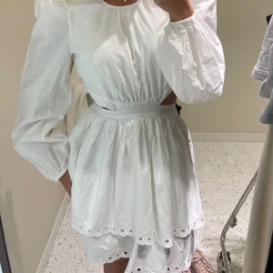 Vit klänning - Charmig vit klänning med långärmade puffärmar och broderade detaljer vid fållen. Den har en markerad midja och en luftig kjol samt öppen rygg. Inga defekter. Använd 1 gång🩷(lånad bild)