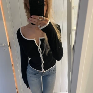 Svart långärmad topp med vita detaljer - Snygg svart långärmad topp med vita kanter och knappar framtill. Perfekt för en stilren look.