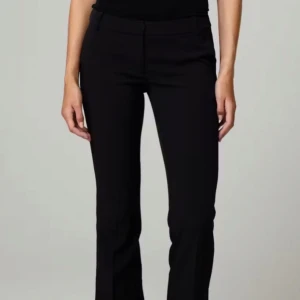 Svarta kostymbyxor - Snygga svarta kostymbyxor med en klassisk bootcut-stil. De är högmidjade och har en stilren design med dragkedja och knappar framtill. Perfekta för en elegant look.