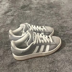 Grå Adidas campus sneakers - Snygga grå Adidas campus sneakers med klassiska vita ränder och snörning. Hyfsat använda vilket dock inte syns på dem då de fortfarande är väldigt fräscha och inte är slitna/trasiga någonstans! 💗Säljer eftersom jag inte använder dem längre