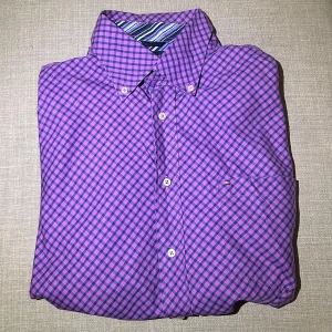 Lila rutig skjorta från Tommy Hilfiger - Snygg lila rutig skjorta från Tommy Hilfiger med klassisk krage och knappar framtill. Perfekt för en stilren look. Skjortan har en diskret ficka på bröstet och är tillverkad i ett bekvämt material.