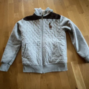 Grå quiltad jacka från Ralph Lauren - Säljer en snygg grå quiltad jacka från Ralph Lauren med bruna detaljer. Jackan är mer utav en vår jacka, den är i XL men sitter bra på mig som är 171 
