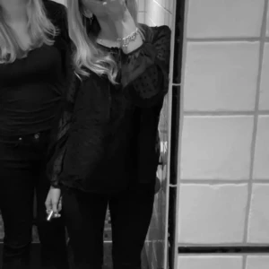 Svart blus från Vila - Elegant svart blus från Vila med prickigt mönster och transparenta långa ärmar. Blusen har en knytning vid halsen och spetsdetaljer vid axlarna. Perfekt för en stilren look.