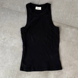 Svart ribbad linnetopp - Snygg svart ribbad linnetopp från Gina tricot. Denna ärmlösa topp har en tight passform och är perfekt för en stilren look. Tillverkad i ett mjukt och stretchigt material som ger en bekväm känsla hela dagen.