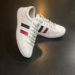 Moncler skor - Snygga vita sneakers från Moncler. Skorna är i väldigt bra skick och det finns inte några stora defekter. Skorna är i storlek 41 men passar 42.     Skick: 8,5/10   Nypris: ca 6000kr