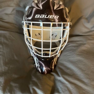 Hockeymask från Bauer - Säljer en cool land hockeymask från Bauer med ett unikt svartvitt mönster. Masken har en vit gallerfront och justerbara remmar för perfekt passform. Perfekt för träningar.