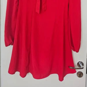 Röd Mini Tie Dress - Snygg röd klänning med knytband vid bröstet och långa ärmar. Perfekt för en färgstark look. Dragkedja i ryggen. Helt ny med prislapp 