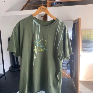 Travis Scott astro world t shirt  - Säljer en grön T-shirt från Astroworld med Travis Scott-tryck. Framsidan har text och grafiska detaljer i blått och gult, medan baksidan har ett stort lila och svart blommönster med texten 'Travis Scott Live'. Perfekt för fans av Travis Scott!  Storlek XL